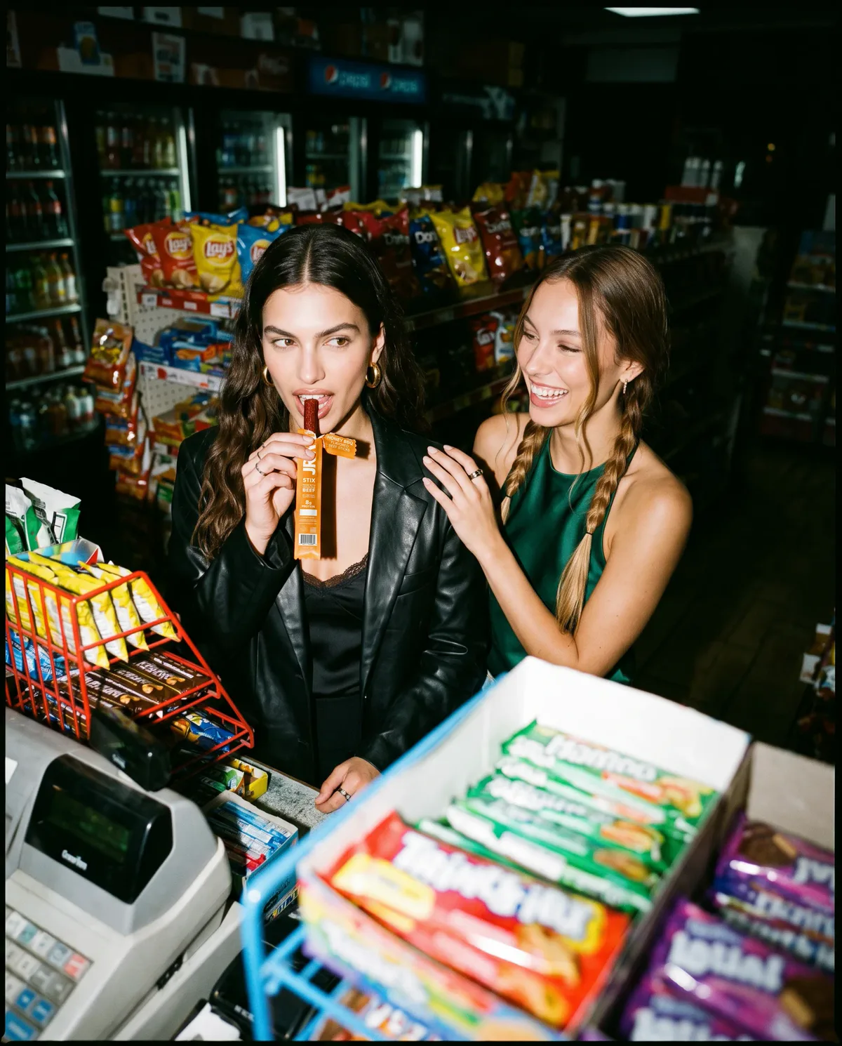 Model biting a beef stick at the checkout counter while her friend laughs