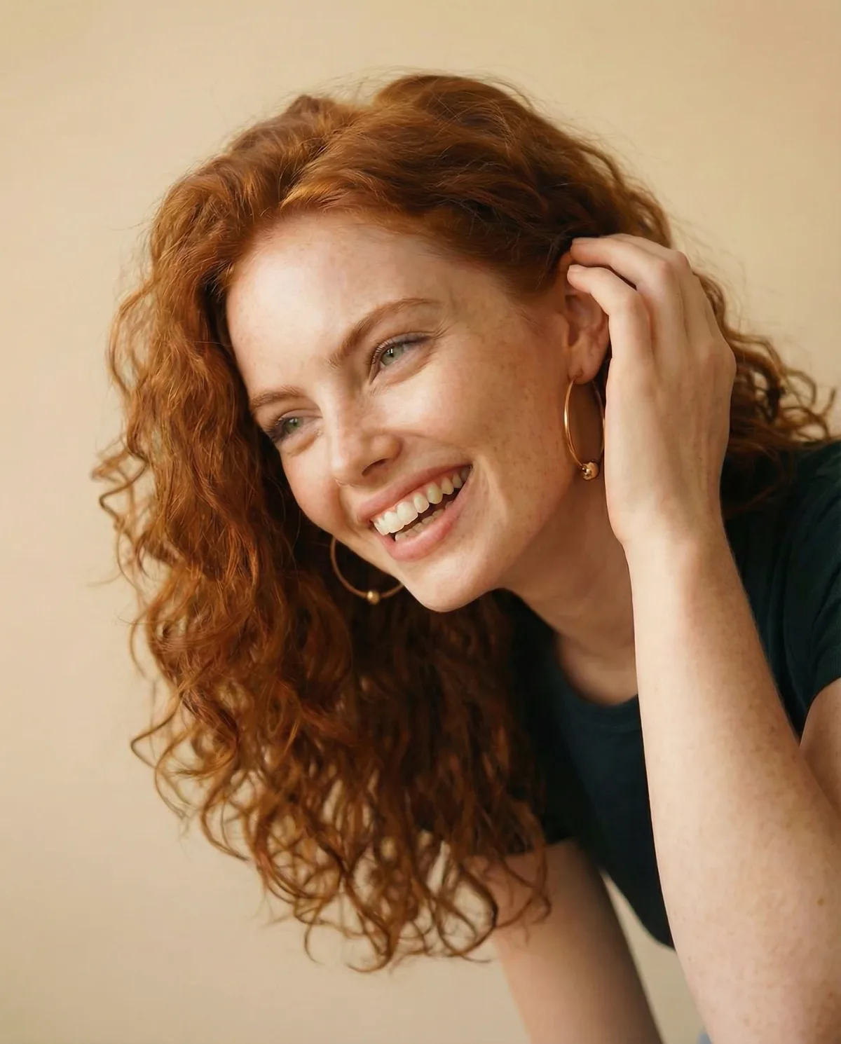 Red-haired model laughing, wearing large gold hoop earrings