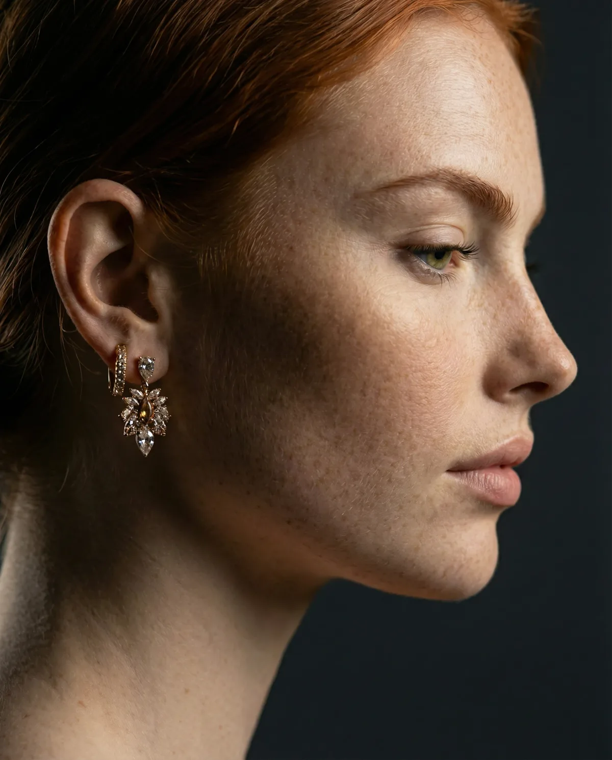 Red-haired model in profile against a dark backdrop, rose-gold cluster earring and pavé huggie
