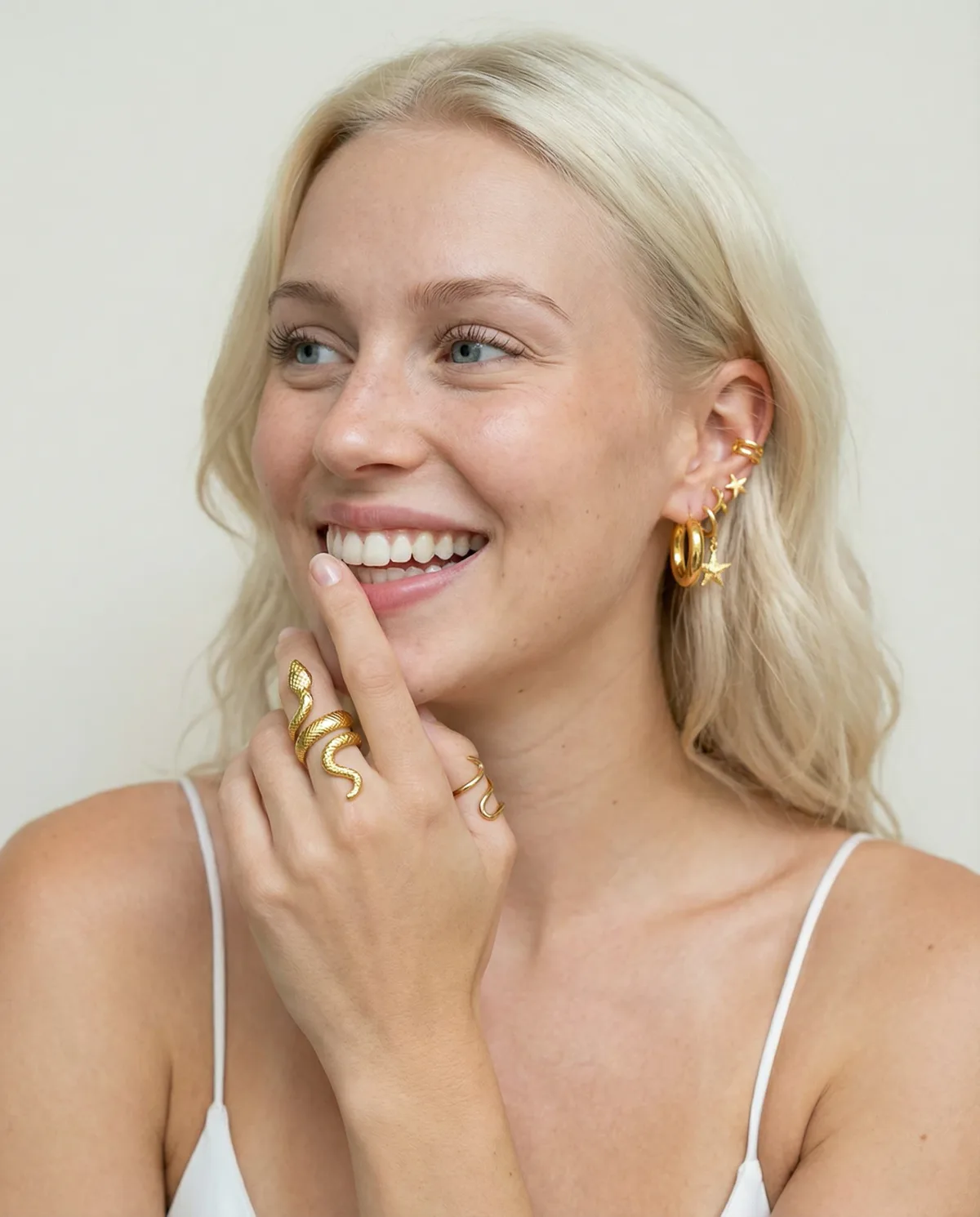 Smiling blonde model wearing a gold snake ring and a stacked gold ear set